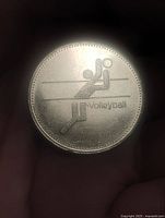 Obverse of coin showing volleyball graphic and text
