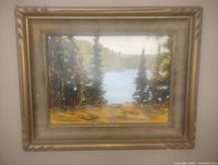 Framed oil painting showing forested lake scene