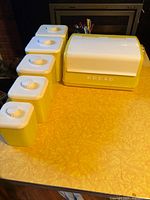 Bread box and five matching yellow canisters on table