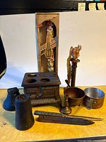 Group shot of all metal items including toy stove, candlesticks, bell, weight, cauldron, cup, letter opener and boxed drip candle
