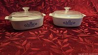Two CorningWare Cornflower Blue casseroles with lids on red background