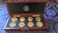 Open presentation case displaying eight gold-plated commemorative coins in capsules