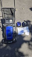 Lawn mower, battery compartment visible, chargers and manuals laid out
