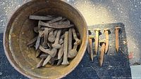 Bucket containing numerous rusty steel railroad spikes with several laid out for size reference.