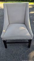 Front view of beige upholstered accent chair showing nailhead trim and wood legs
