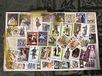Album page filled with about 55 worldwide stamps featuring folk costumes, cellophane tape across upper left, visible tape staining and worn page edges