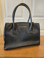 Front view of Christian Siriano black leather handbag on table
