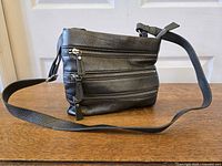 Side view showing pebbled leather texture, adjustable strap, three front zip pockets