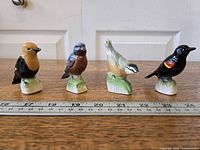 Group shot of four ceramic bird figurines with ruler showing scale