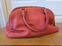 Full side view of red pebbled leather satchel showing handles and shape