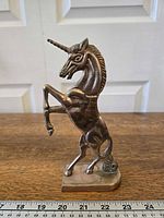Front three-quarter view of brass unicorn on base with ruler for scale