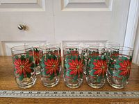 Front view of 10 poinsettia glasses aligned behind ruler