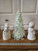 Full view of two ceramic angel figurines flanking feather tree with ruler for scale