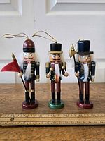 Front view of three wooden nutcracker ornaments with ruler for scale