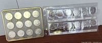 Two coin sets: one in a black display case and one in clear plastic coin holders.