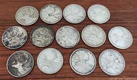Top view of 13 Canadian silver quarters laid out on a wooden surface showing obverse and reverse sides with visible tarnish and wear.