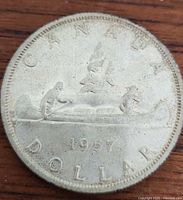 Close-up photo of 1957 Canadian silver dollar coin showing the Voyageur design with two men paddling a canoe and the date 1957 clearly visible.