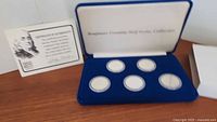 Blue presentation case open with five clear capsules each holding a silver half dollar coin, arranged in two rows, with a card showing Benjamin Franklin and introduction text.