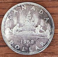 Obverse side of the 1962 Canadian silver dollar coin showing the canoe design with two figures and tree.