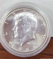 Obverse side of 1964 silver half dollar coin showing profile of John F. Kennedy, dated 1964, in protective plastic case.