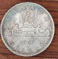 Reverse of the 1965 Canadian silver dollar coin showing the canoe design with two paddlers and a tree in the background marked 'CANADA DOLLAR 1965'.