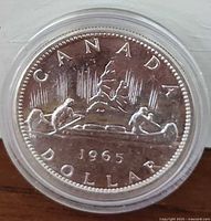Reverse (back) of 1965 Canadian Silver Dollar Coin featuring the Voyageur canoe design and denomination, in protective case.