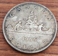 Full obverse side of the 1966 Canadian silver dollar coin showing canoe design with paddlers and trees.
