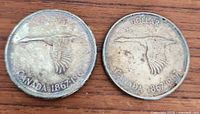 Two silver-colored Canadian dollar coins side by side on wooden surface, both featuring a flying goose and dated 1867-1967.