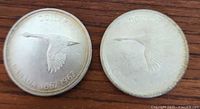 Two Canadian silver dollar coins side-by-side on a wooden surface showing the flying goose and the dates 1867-1967.