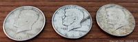 Three 1964 Kennedy half dollar coins laid out side by side showing obverse sides with Kennedy's profile and inscriptions.
