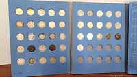 42 silver dimes of different designs and conditions arranged in a blue coin album with some slots empty.