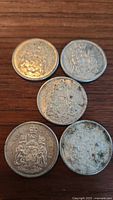 Top view of 5 Canadian silver half dollar coins showing the detailed coat of arms on one side with visible wear and tarnishing.