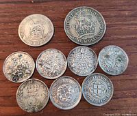Top-down view of 9 silver British coins showing obverse and reverse details on wood surface.