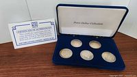 Overview of Certificate of Authenticity and open blue presentation box containing six Peace Dollars in velvet tray