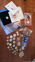 Mixed lot of coins on wooden surface including coins in plastic holders, coin sets, and packaging.