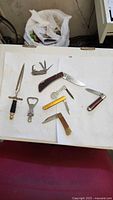 Group view of all knives, bottle openers, letter opener and token