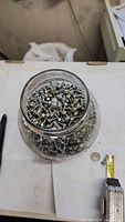Top view of open glass jar packed with silver steel screws