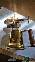 Side view of brass blow torch showing burner assembly, fuel tank and wooden handle