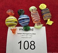 Four Murano glass candies on red background with lot card