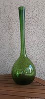 Full view of green glass bottle vase standing on wood surface