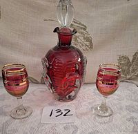 Front view of ruby red Aseda decanter with stopper flanked by two stemmed glasses