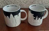 Front view of both skyline mugs showing city names inside rims
