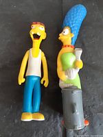 Front view showing both Simpsons figurines: Marge with trash can, male character in tank top