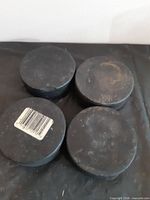 Four black hockey pucks laid flat, one with barcode sticker