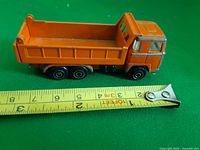 Left side view of orange dump truck next to measuring tape showing length