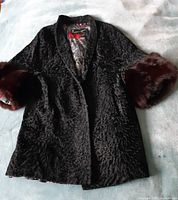 Front view of black Persian lamb coat with burgundy fox fur cuffs attached