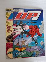 Front covers of both DP7 comics, blue Issue on top, yellow Issue behind