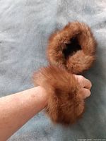 Hand holding one brown fur cuff showing size and pile