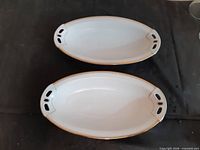 Two white porcelain oval dishes with gold trim viewed from top