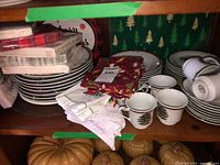 Stacked Christmas tree pattern plates, cups, cloth napkins, paper napkins on shelf